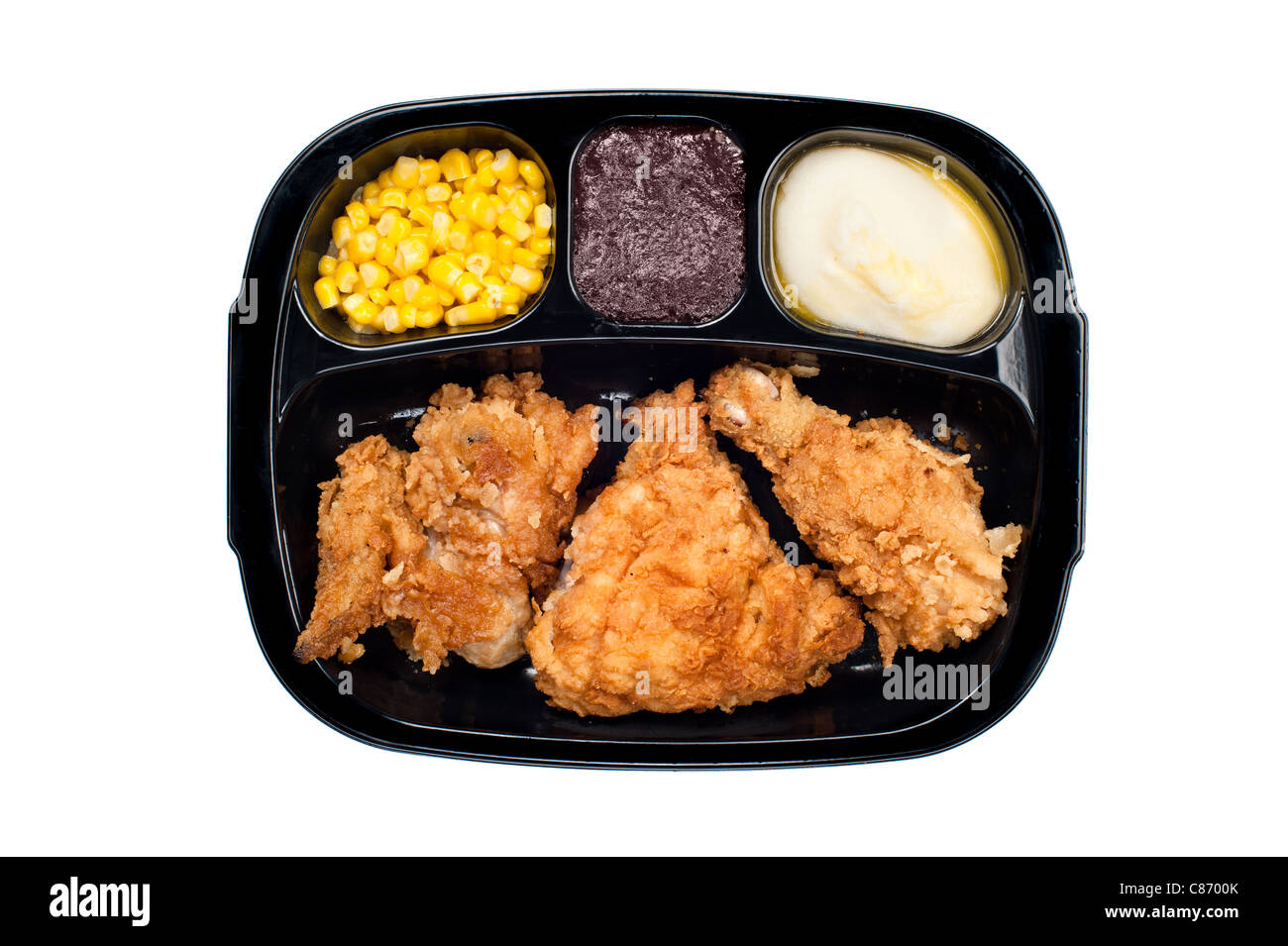 A cooked tv dinner of fried chicken, corn, mashed potatoes and dessert in a plastic black tray. Stock Photo