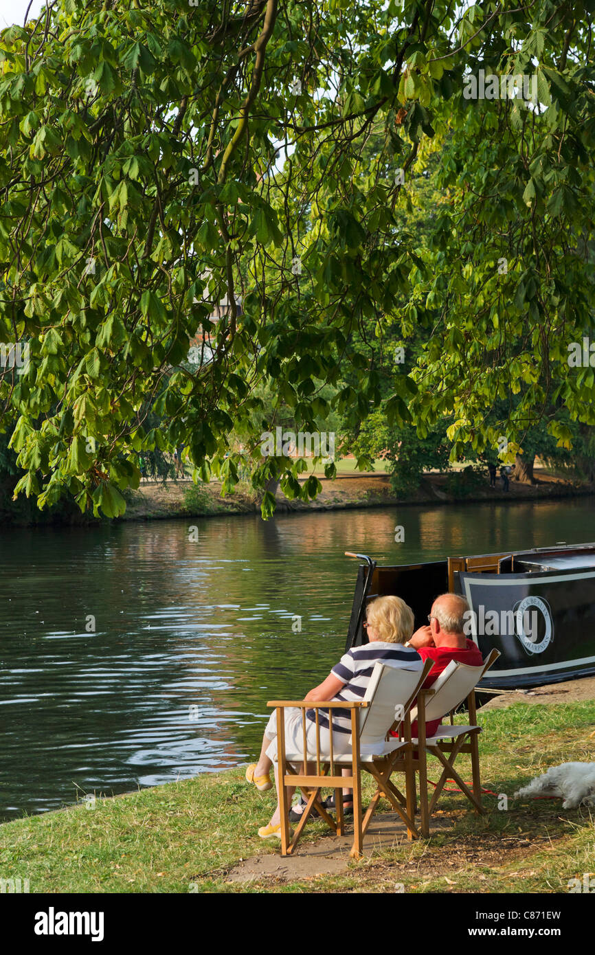 Couple sitting by their narrowboat on banks of River Avon in late afternoon sun, Stratford-upon-Avon, Warwickshire, England, UK Stock Photo