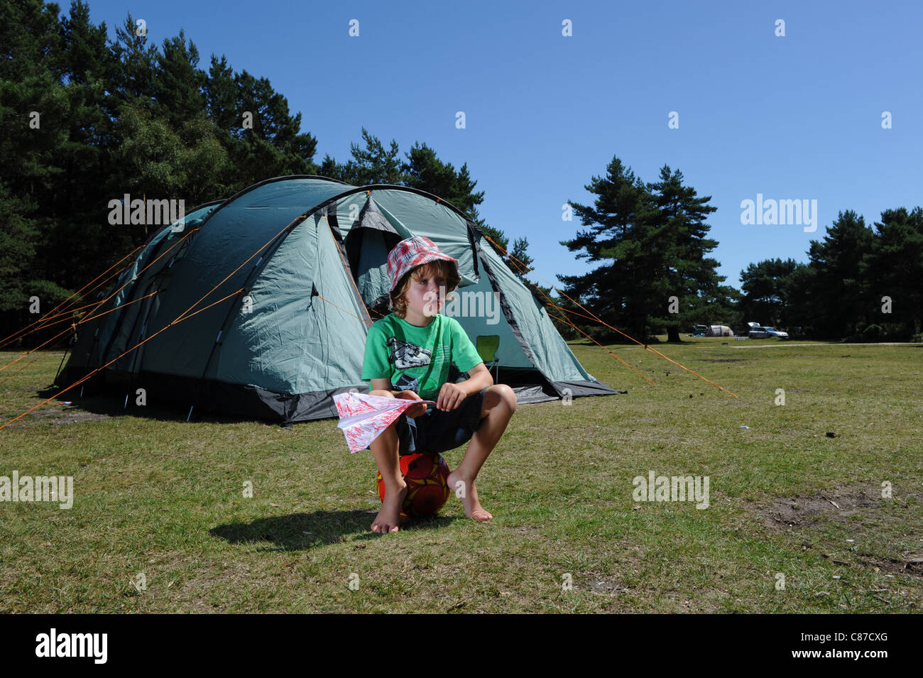 a young boy rests siting  on a football with a paper aeroplane during a camping holiday enjoying the sun Stock Photo