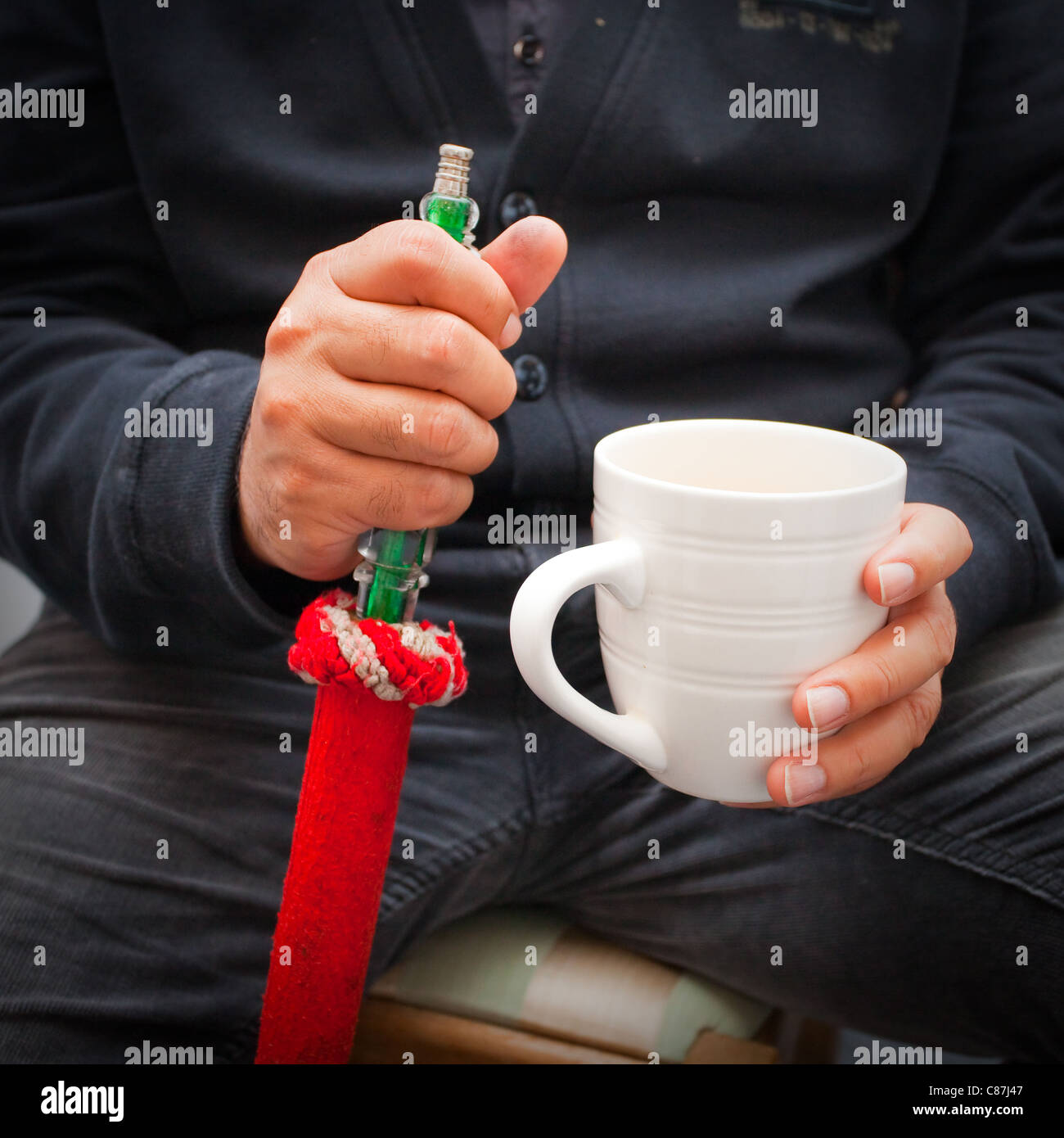 Close up of an unidentifiable man smoking a shisha pipe and holding a mug of tea Stock Photo