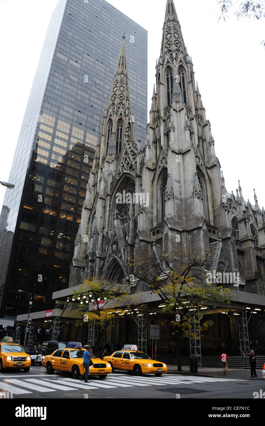 Autumn portrait grey marble spires St.Patrick's Cathedral rising above yellow taxis pedestrian crossing, 5th Avenue, New York Stock Photo