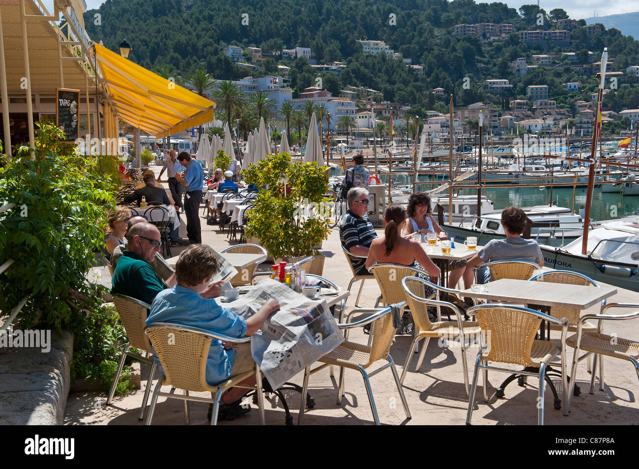 Port Soller harbour cafe restaurant bar terrace with visitors relaxing enjoying the coastal marina sun Palma de Mallorca Spain Stock Photo