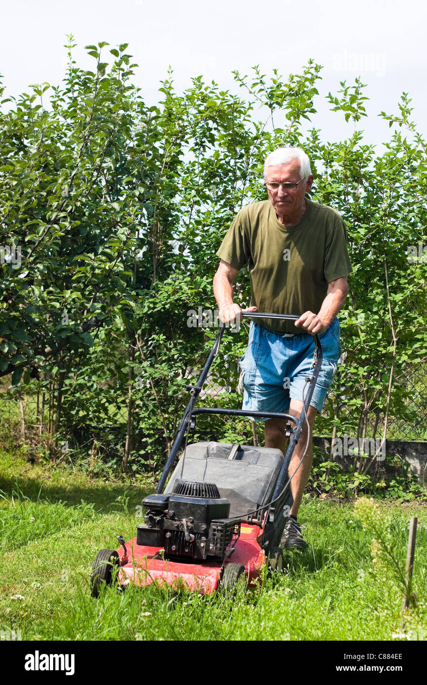 Portrait of elderly man mowing lawn in the garden. Stock Photo