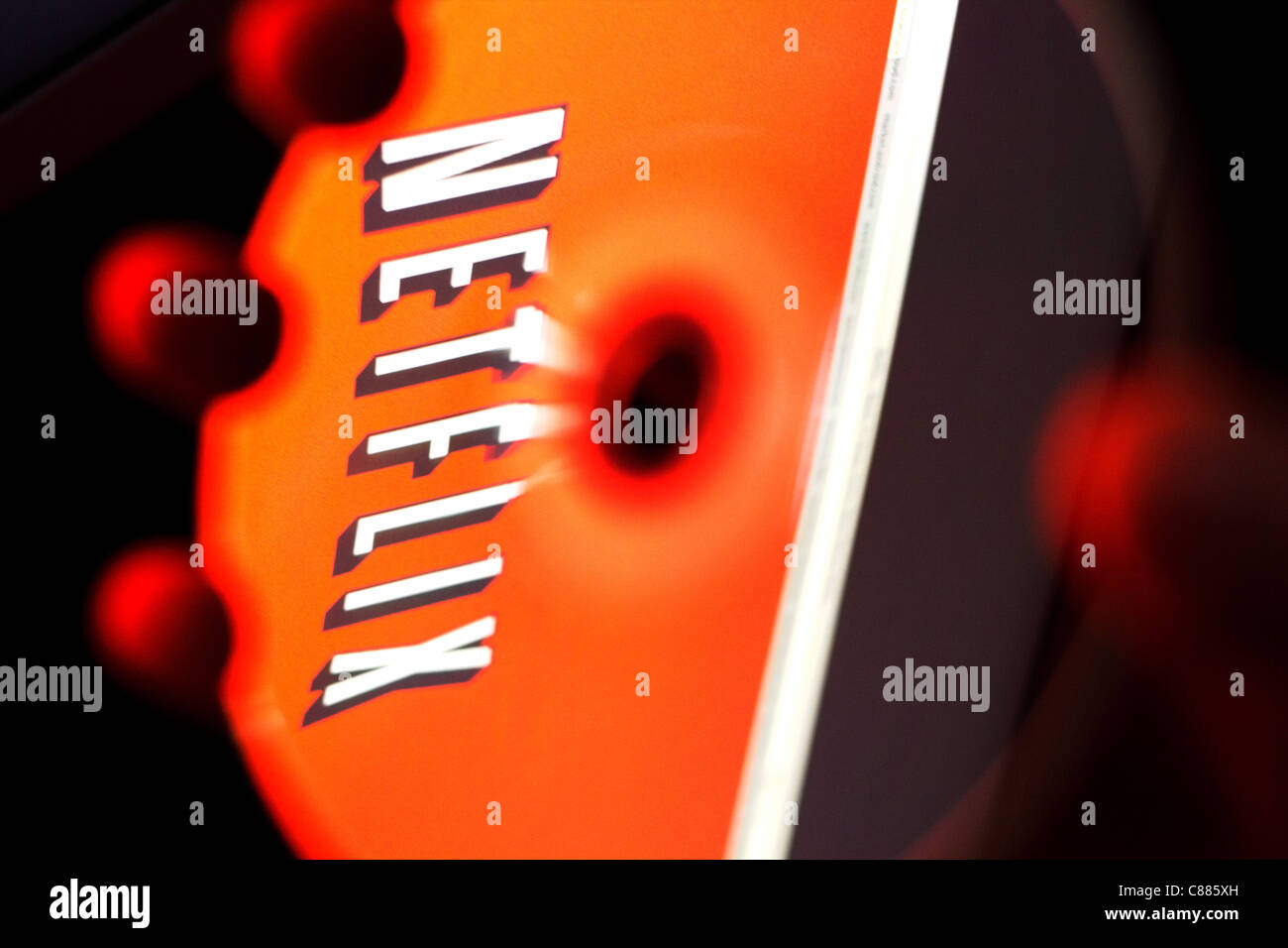 Netflix logo reflected in DVD disc. Hand holding disc in front of Netflix home web page. Stock Photo
