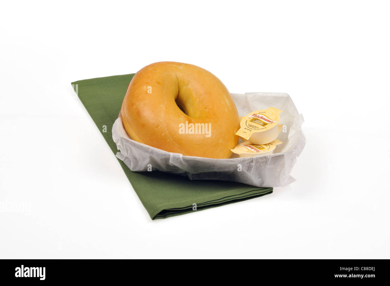Plain bagel with 2 butter containers and knife in a paper basket on with green napkin on white background, cutout. Stock Photo