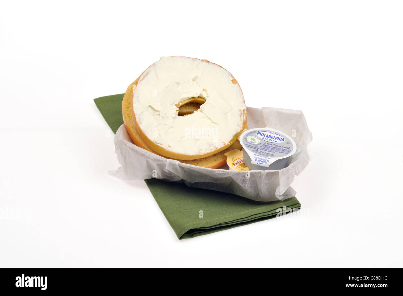 Plain bagel with philadelphia cream cheese containers in a paper basket with green napkin on white background, cut out. Stock Photo
