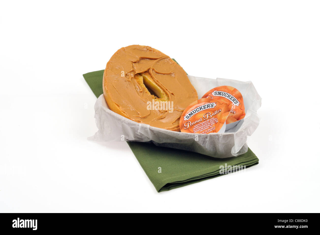 Plain bagel covered  with peanut butter spread and 2 containers of smuckers in a  paper basket  on white background, cutout. Stock Photo