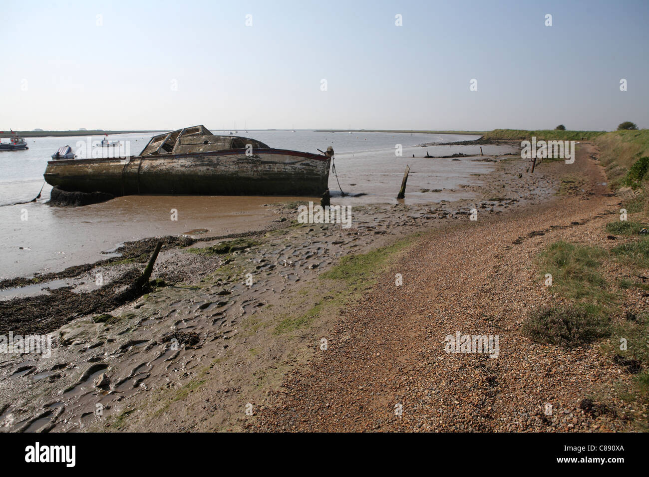River Ore / Alde, bank / wall at Orford Suffolk, UK showing abandoned wooden boat in background Stock Photo
