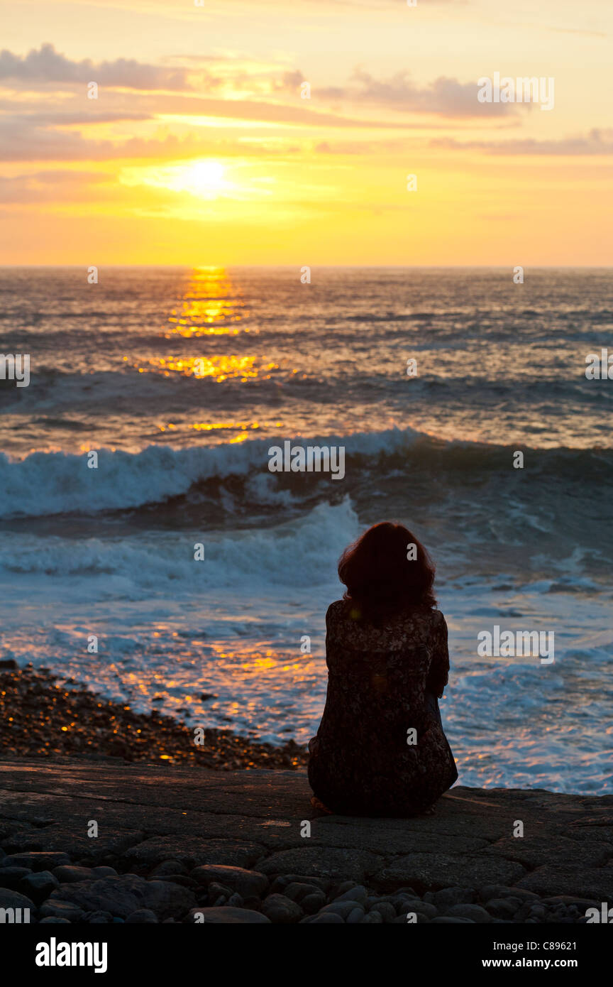 Women sitting watching the sea at sunset Stock Photo - Alamy