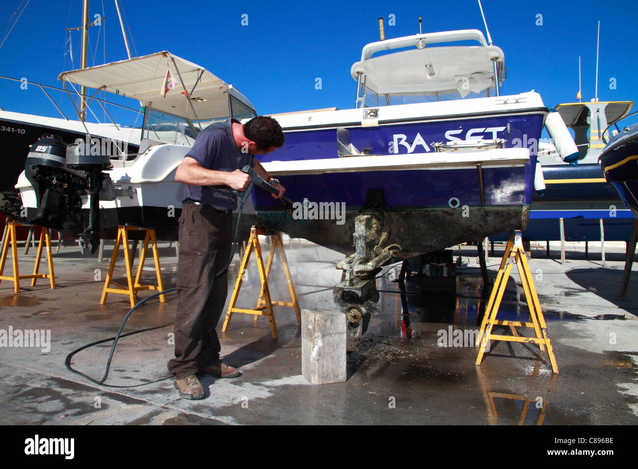 Seaman cleaning his boat´s hull with high pressure water pistol Stock