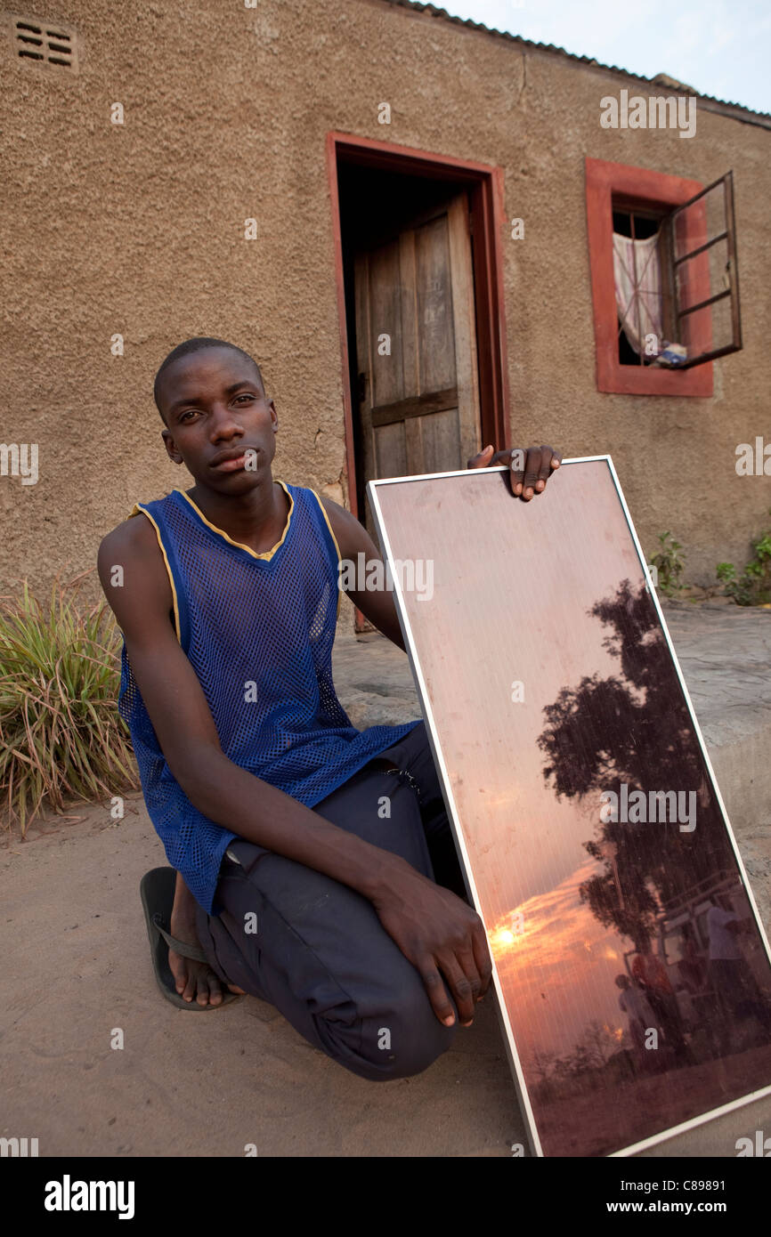 A young man displays a solar panel he uses for charging batteries and lighting his home in Mongu, Zambia, Southern Africa. Stock Photo