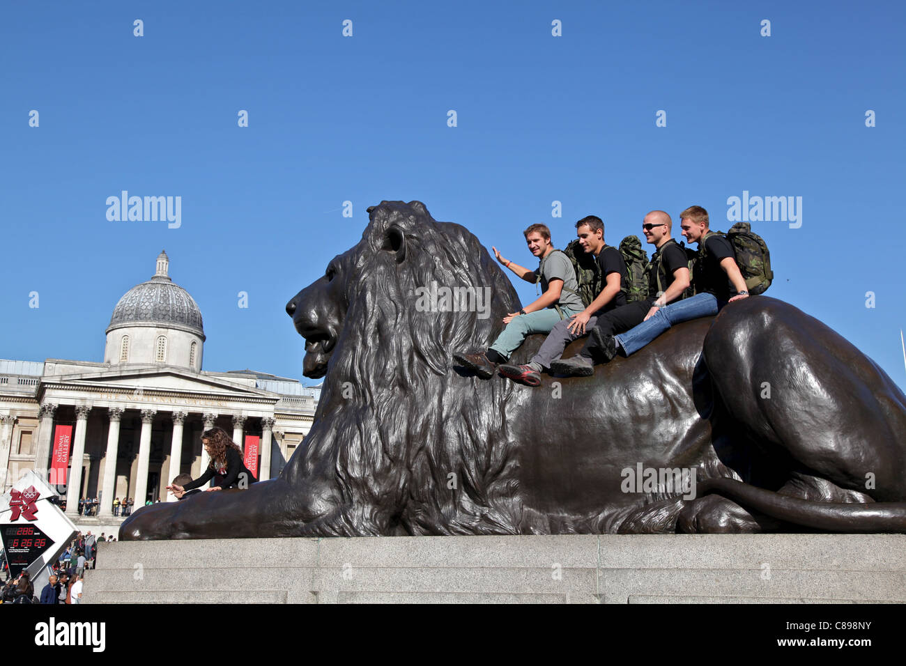 Tourists 'riding' one of the lions at the base of the Nelson's Column monument Stock Photo