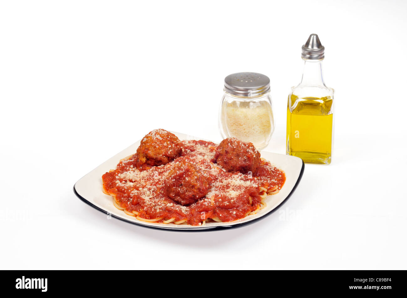 Meal of spaghetti and meatballs with tomato sauce and grated Parmesan cheese on plate on white background with jars of olive oil and cheese. Stock Photo