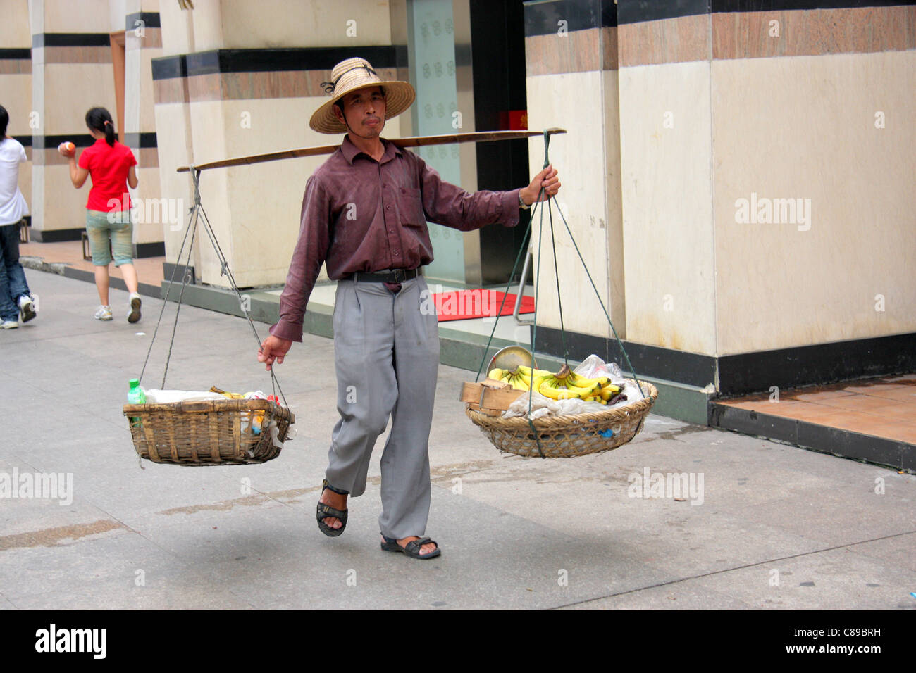 Man using a carrying pole across his shoulders to transport baskets of bananas and other goods, Wuhan, China Stock Photo