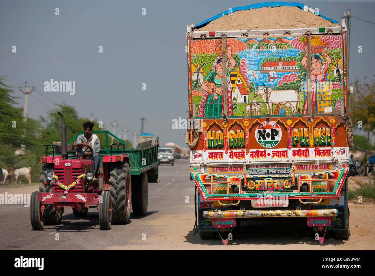 Indian farmer drives tractor past Tata trucks at Rasulpura in Sawai Madhopur, Rajasthan, Northern India Stock Photo