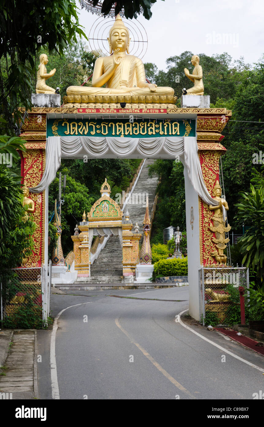 Large entrance arch with a gold Buddha sculpture on top over road at