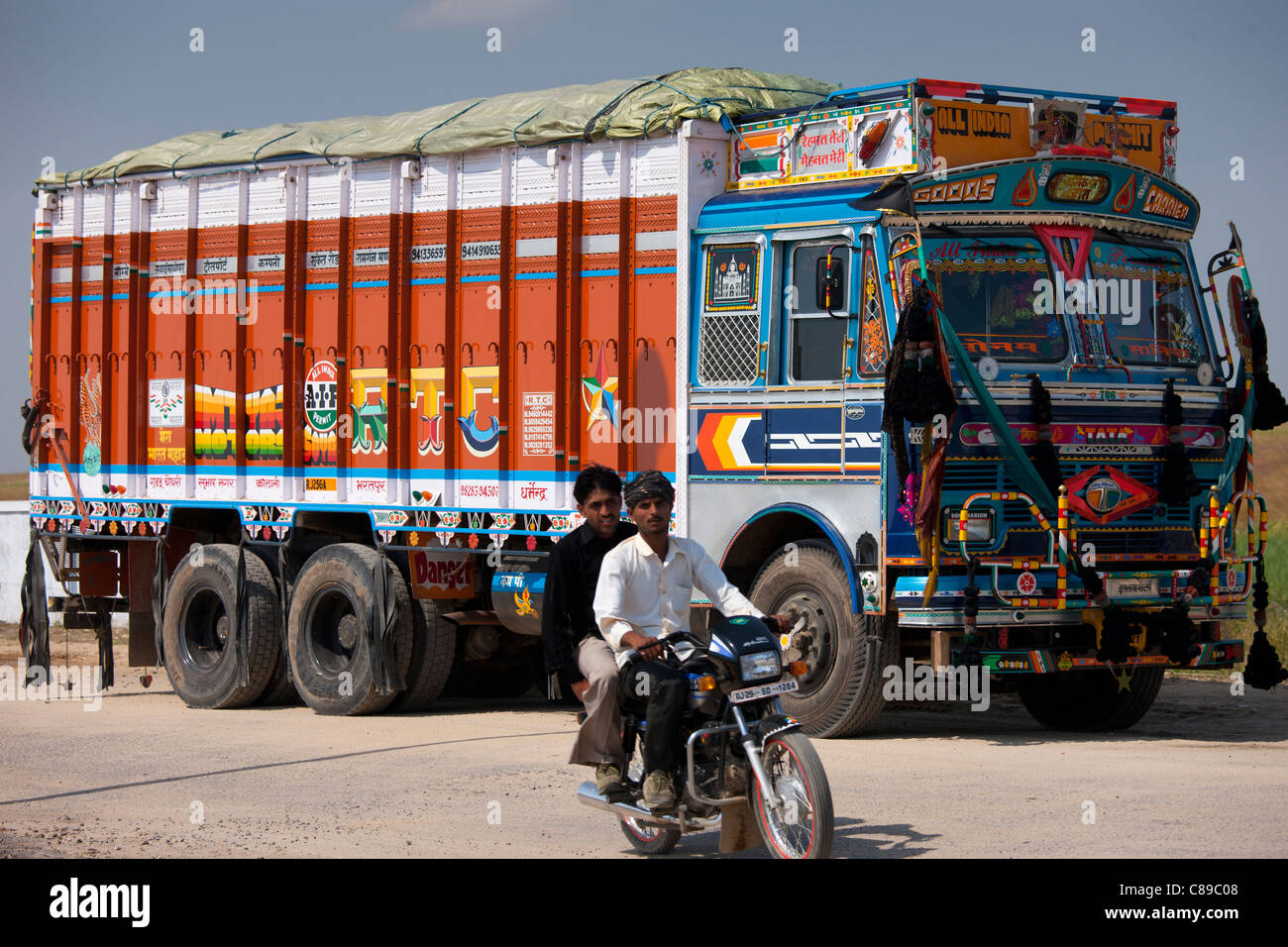 Indian motorcyclist rides past Tata trucks at Rasulpura in Sawai Madhopur, Rajasthan, Northern India Stock Photo