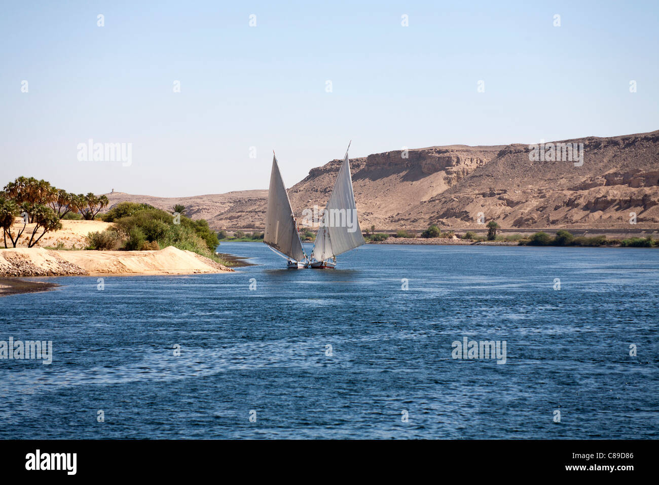 Two Nile fellucas sailing to camera in tandem one tied to the other, rounding a bend in the river with mountains in background Stock Photo