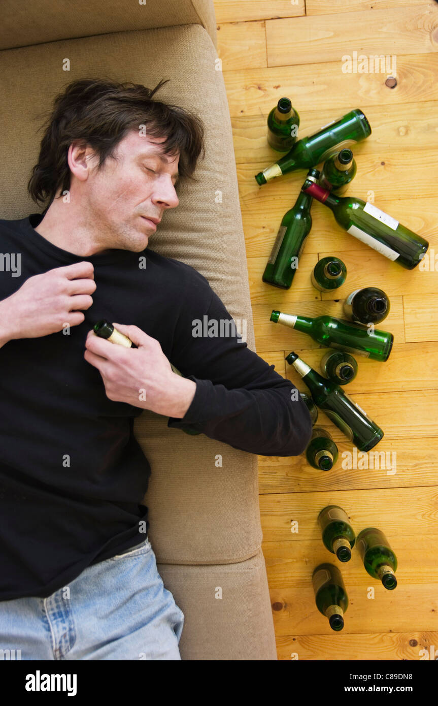 Germany, Hessen, Frankfurt, Drunk man lying on sofa with empty beer bottles Stock Photo
