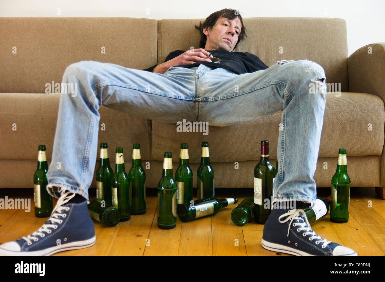 Germany, Hessen, Frankfurt, Drunk man lying on sofa with empty beer bottles Stock Photo