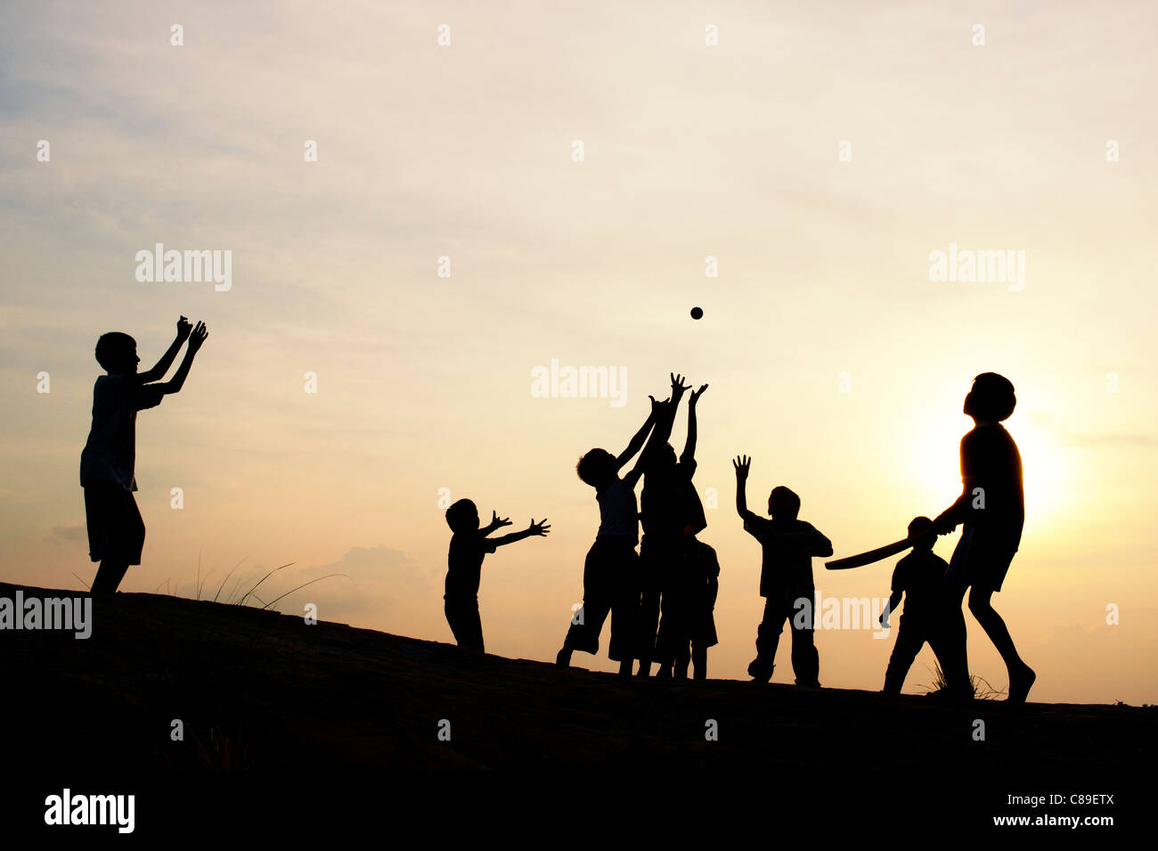 Silhouette of young Indian boys playing french cricket at sunset in India Stock Photo