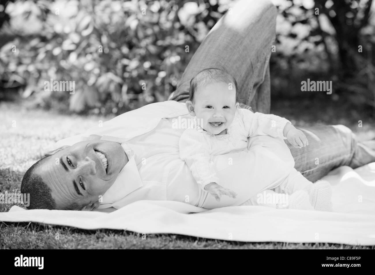 Germany, Bavaria, Father and daughter lying on blanket in garden, portrait, smiling Stock Photo