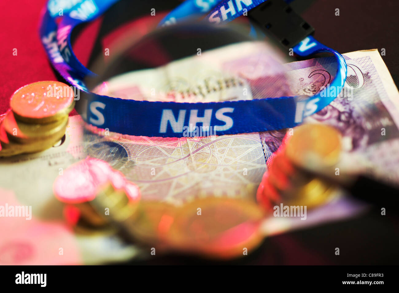 NHS staff neck chain laying on twenty pound notes magnified with pound coins Stock Photo