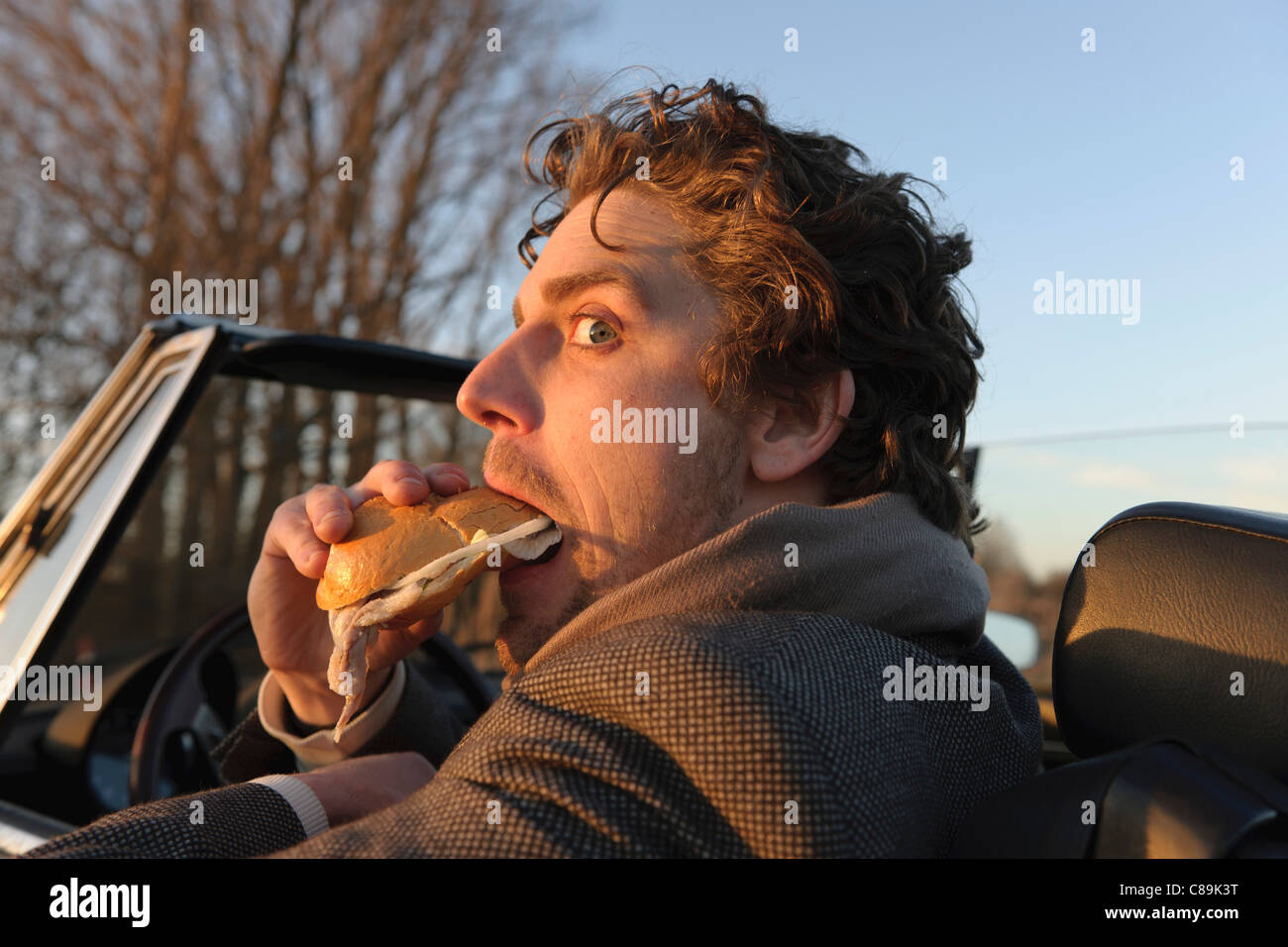 Germany, Hamburg, Man eating fish sandwich in classic cabriolet car Stock Photo