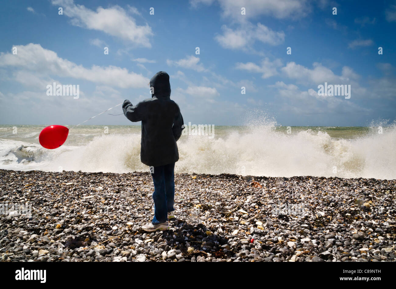 Young child with red ballon on pebble beach Stock Photo