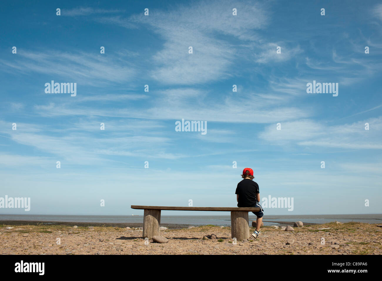 Young boy sitting alone on bench at seaside Stock Photo
