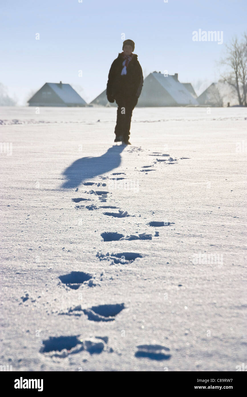 Germany, Vechelde, Boy walking in snow with footprints in foreground Stock Photo