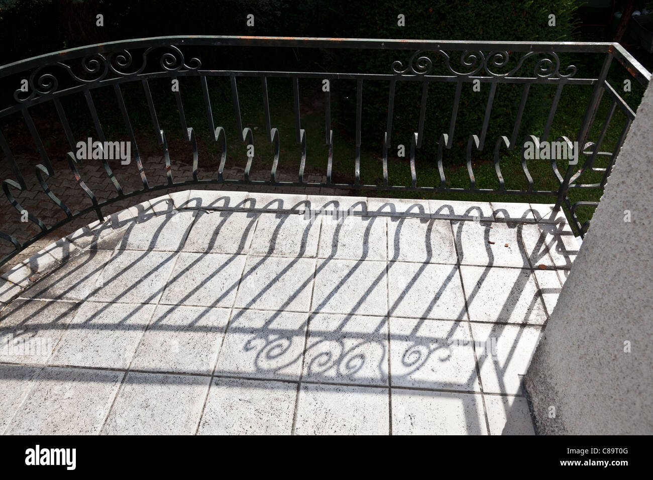 Shadow of ornate metal railings on floor of balcony of French house a summer's day Stock Photo