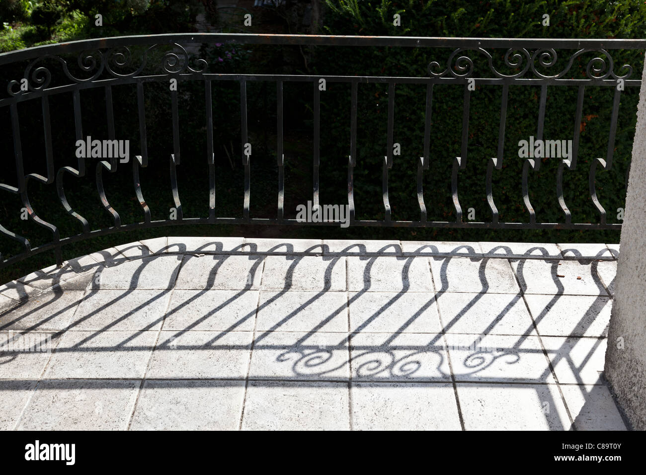 Shadow of ornate metal railings on floor of balcony of French house a summer's day Stock Photo