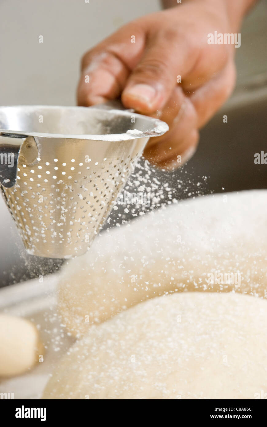 Flouring with a sieve the uncooked bread loaves Stock Photo