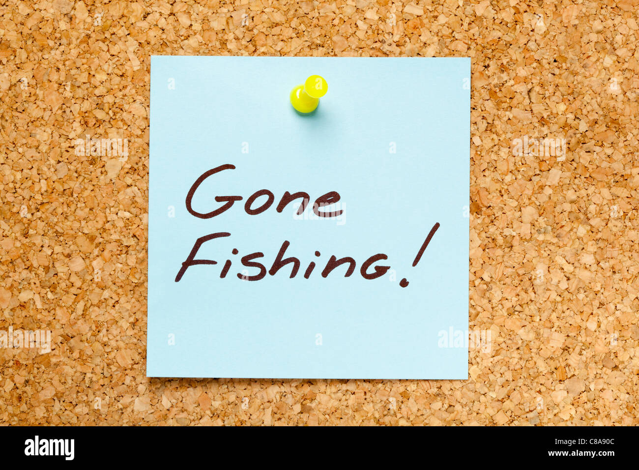 GONE FISHING! written on a blue sticky note on an office cork bulletin board. Stock Photo