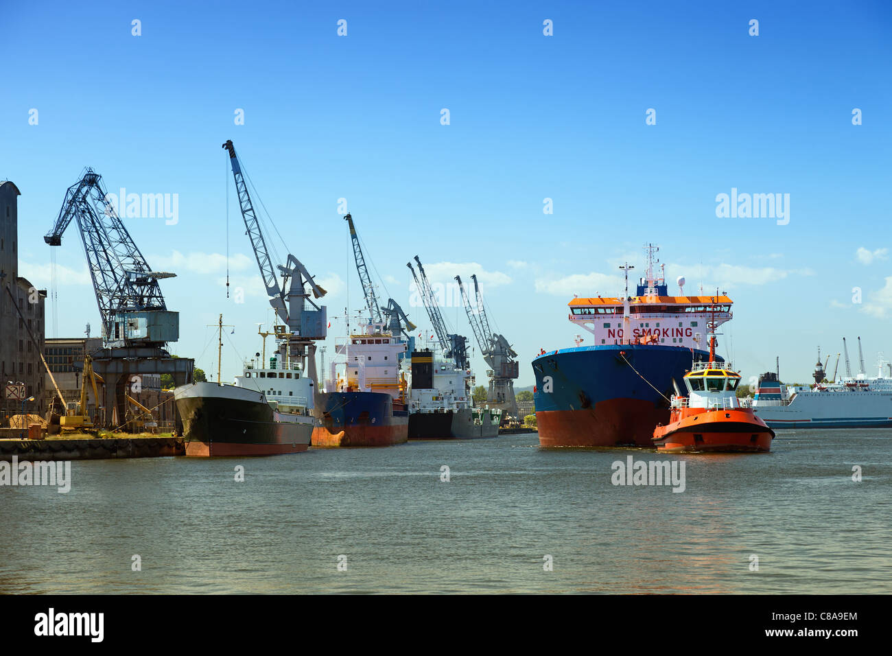A large cargo ship enters the port escorted by tugboats. Gdansk, Poland. Stock Photo