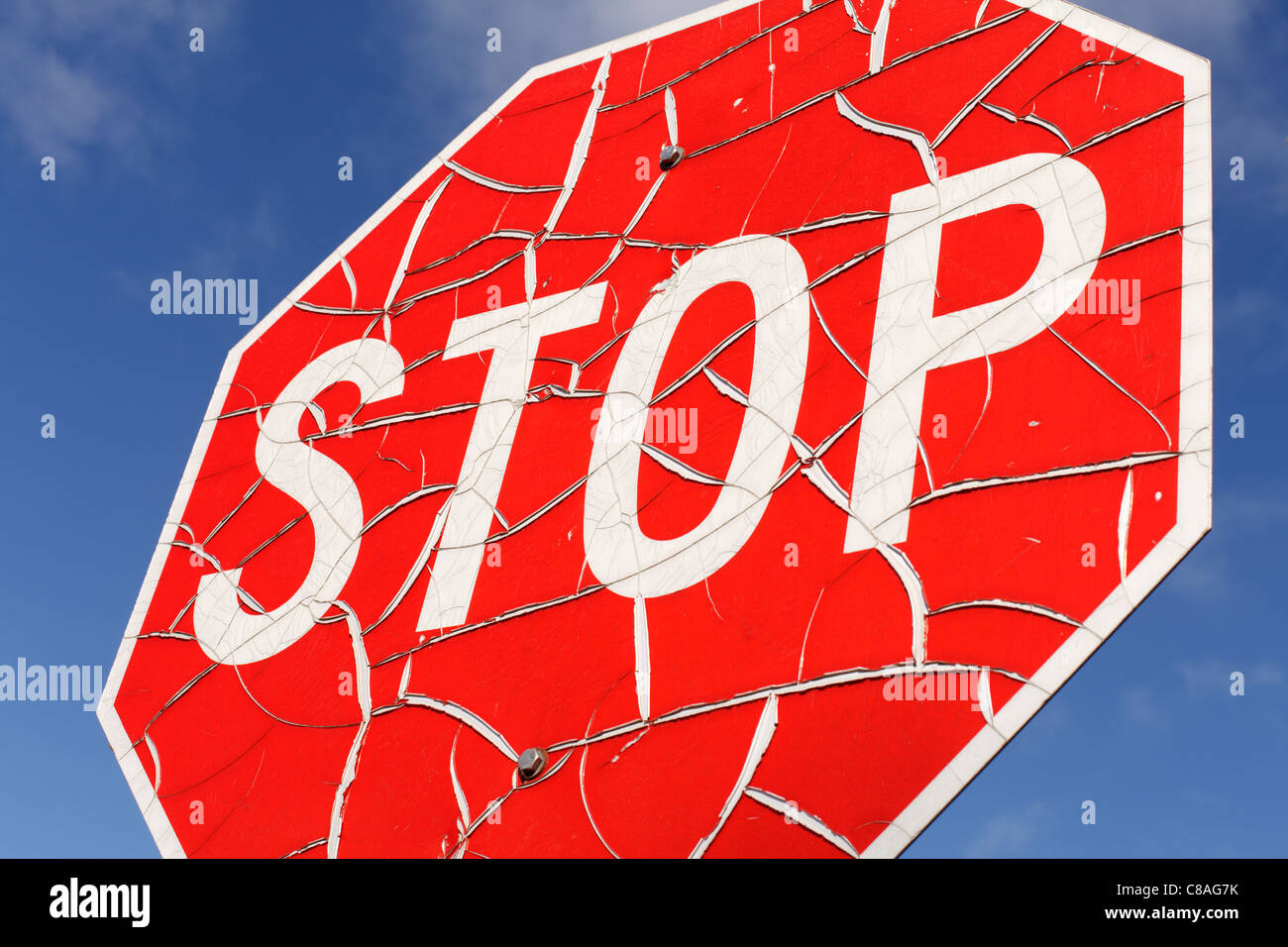 A cracked and worn stop sign against blue sky. Stock Photo