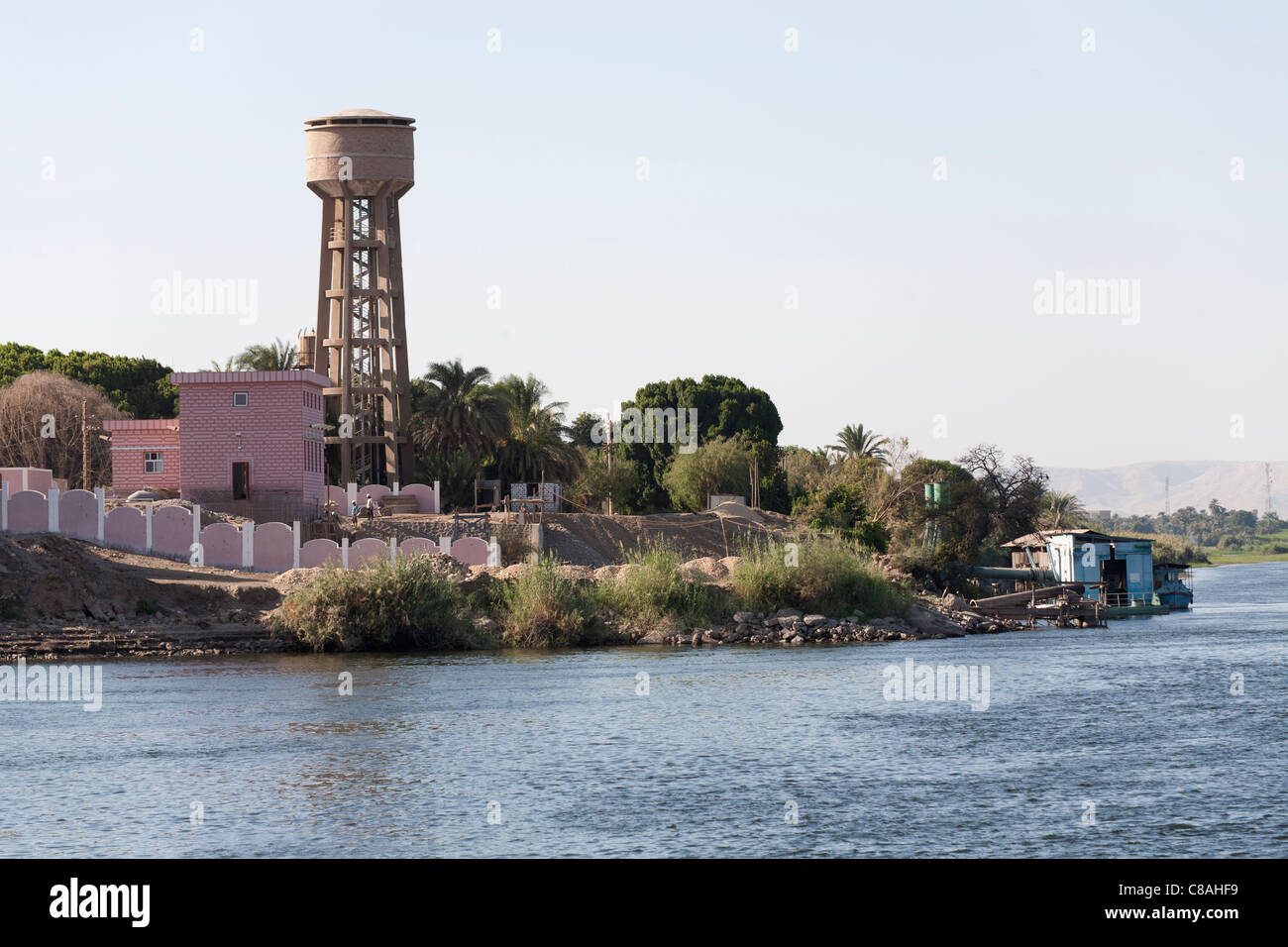 Section of Nile river bank with official buildings painted pink  and large water tower near water's edge, Egypt, Africa Stock Photo