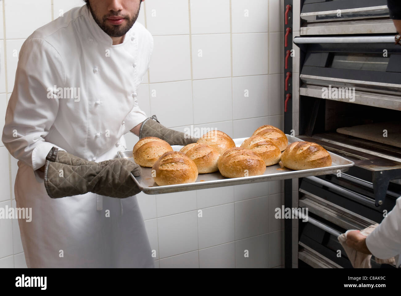 Cook taking the bread loaves out of the oven Stock Photo