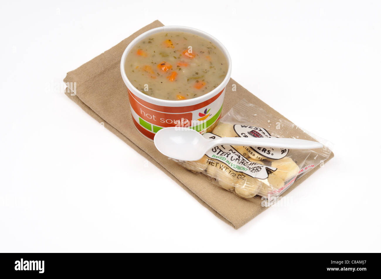 A take away cup of potato and leek soup with a spoon & oyster crackers on white background, cut out. Stock Photo