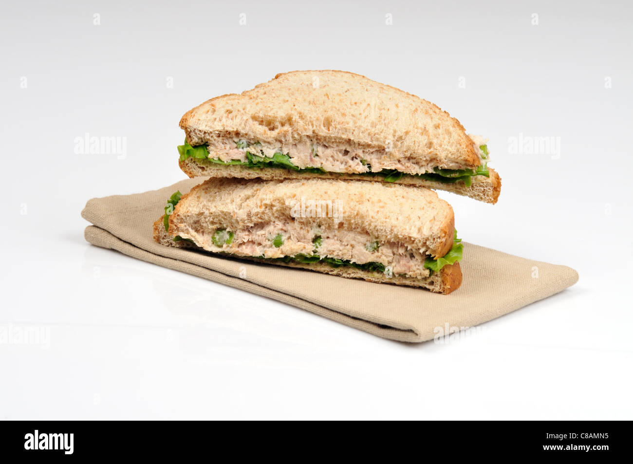 Tuna mayo sandwich with lettuce made with wholemeal bread cut in half and stacked on white background, cutout. Stock Photo