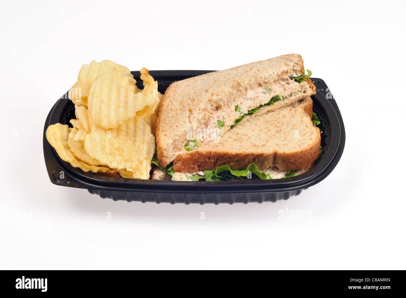 Tuna mayo sandwich with celery & lettuce on wholemeal bread cut in half w/ crisps or potato chips in a take away black plastic tray on white, cutout. Stock Photo
