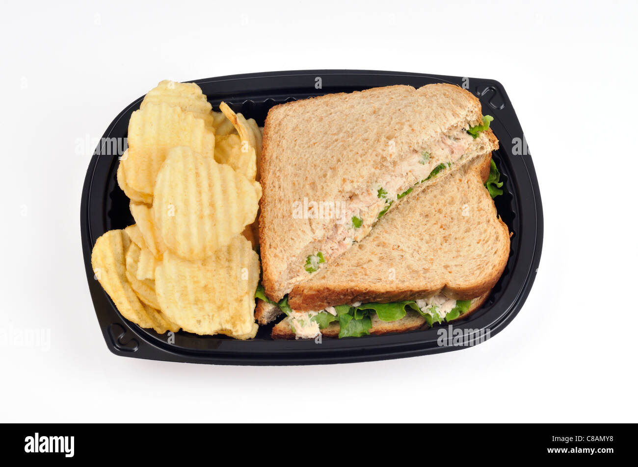 Tuna  mayo sandwich with lettuce made with wholemeal bread cut in half with ridged potato chips in a takeaway plastic container on white, cutout. Stock Photo