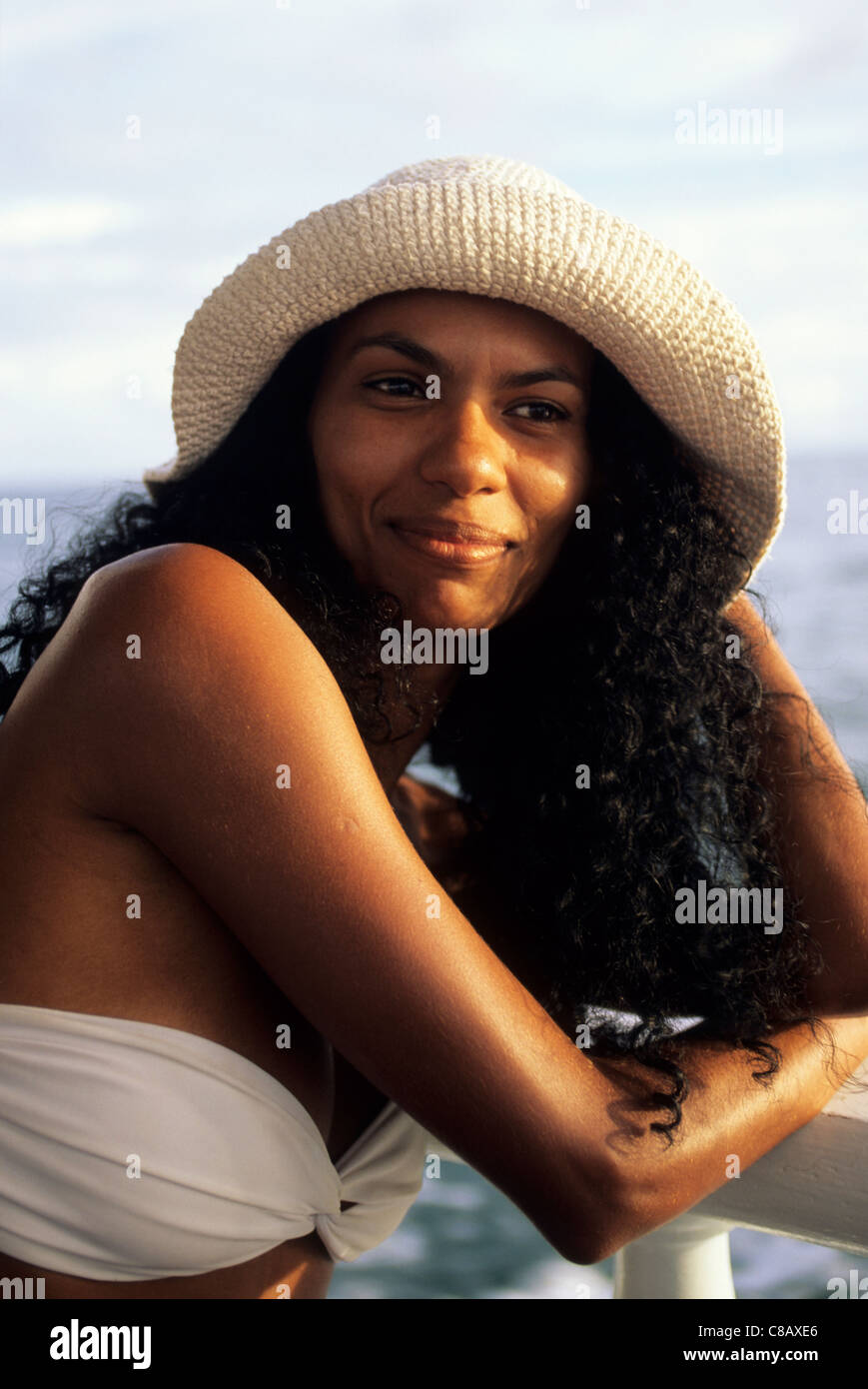 Bahia, Brazil. Smiling young woman with curly black hair in a straw sunhat and white strapless bikini. Stock Photo