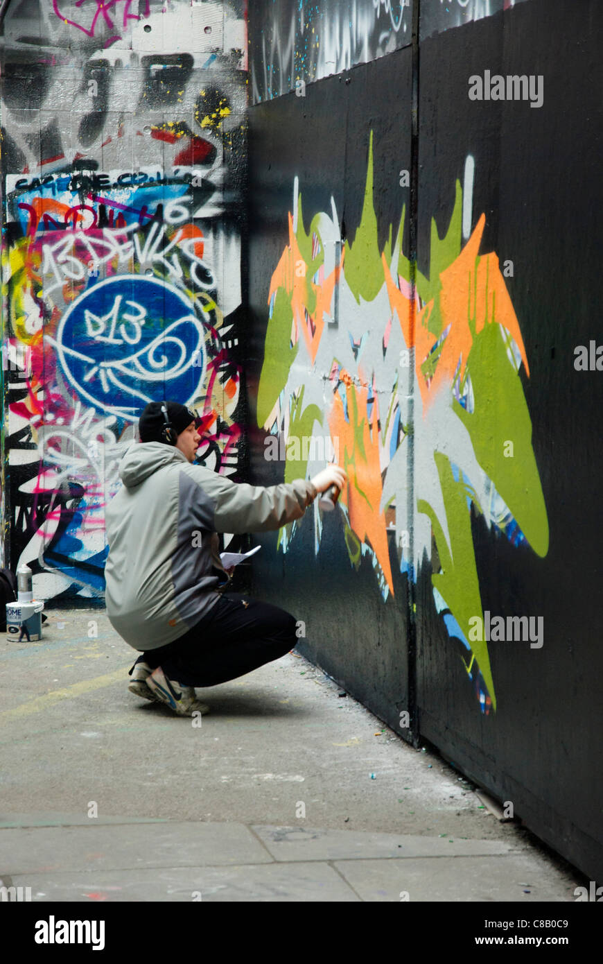 Graffitti artist at work on South Bank, London wearing a pair of headphones Stock Photo