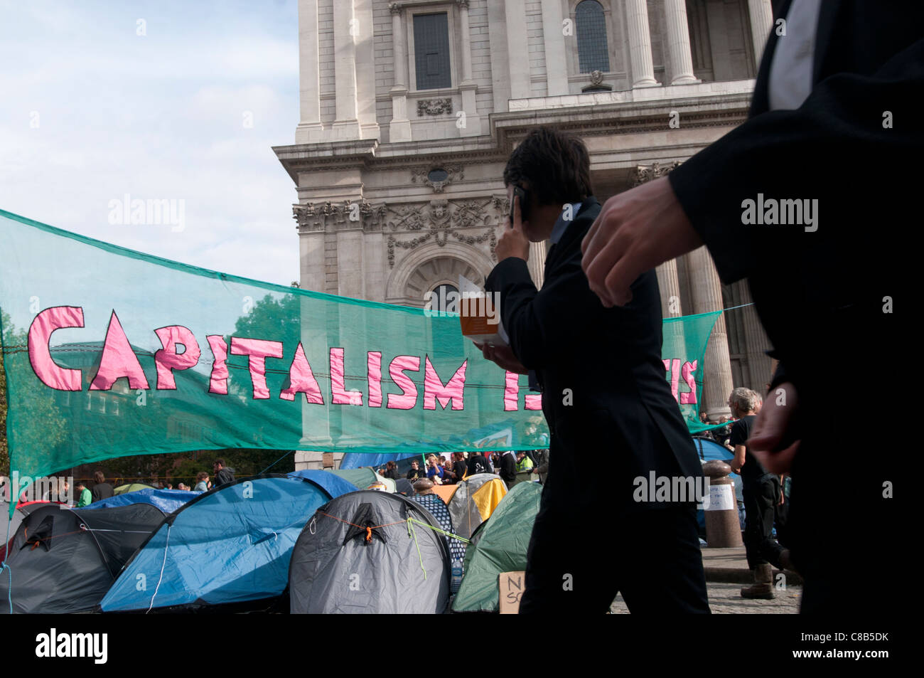 Occupy London in front of St Paul's. Part of worldwide protest .City workers pass by the camp and banner saying capitalism. Stock Photo