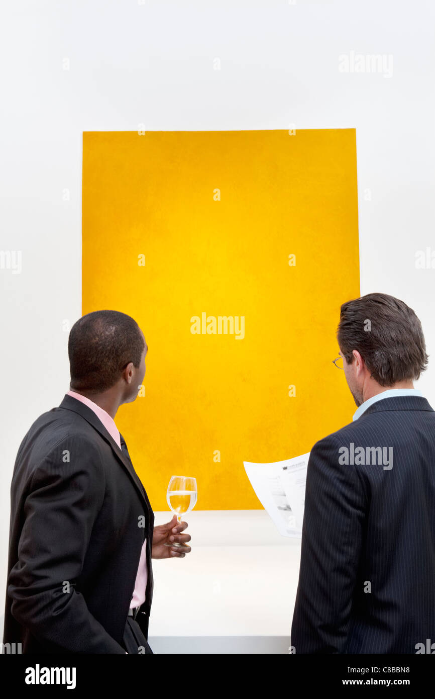 Two people looking at yellow painting on wall in art gallery Stock Photo