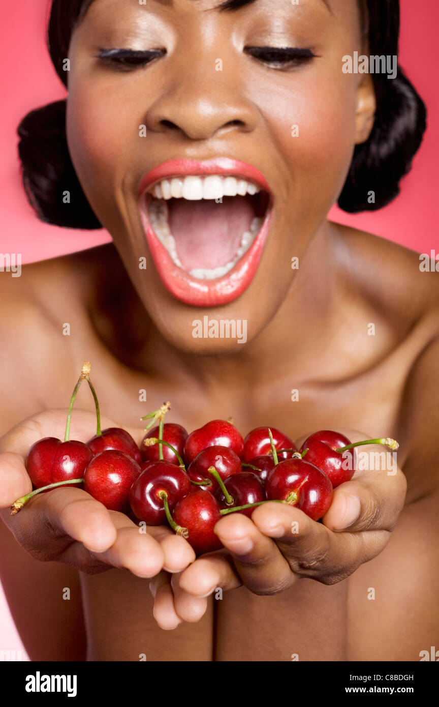 Cheerful young woman looking at cherry in her hands Stock Photo