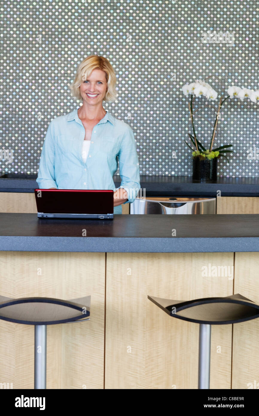 Portrait of smiling woman using laptop in kitchen Stock Photo