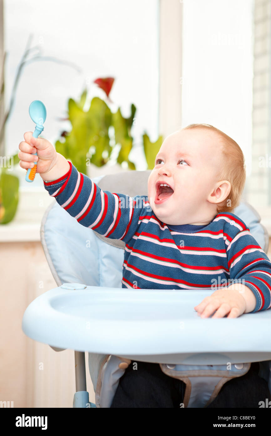 Little kid sitting in highchair and waving his spoon. Expression during